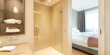Modern hotel room with a view of the bathroom: shower, washbasin, towels and bedroom with double bed.