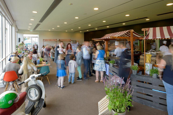 Menschen genießen ein Buffet in einem hellen Raum mit Marktständen im ATLANTIC Hotel Galopprennbahn Bremen.