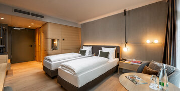 Modernes Hotelzimmer mit zwei Einzelbetten, stilvoller Beleuchtung, Sitzbereich und Holzakzenten im ATLANTIC Hotel Heidelberg.