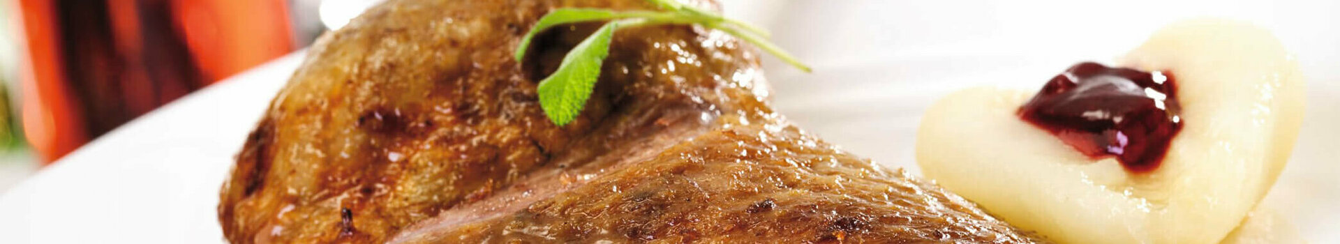 Gans ATLANTIC in den ATLANTIC Hotels in Bremen, Bremerhaven, Kiel, Lübeck, Travemünde und Wilhelmshaven Gebratene Entenkeule mit Bratensauce, garniert mit Kräutern, serviert mit Kartoffelpüree und Preiselbeeren auf weißem Teller.