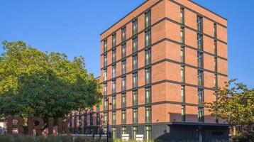 unique by ATLANTIC Hotels Bremen Backsteinhotel mit modernen Fenstern, umgeben von Bäumen und einem großen, grünen Innenhof bei klarem Himmel.