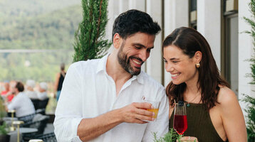 Couple enjoying drinks on the terrace of the ATLANTIC Hotel Heidelberg with a view of green hills.