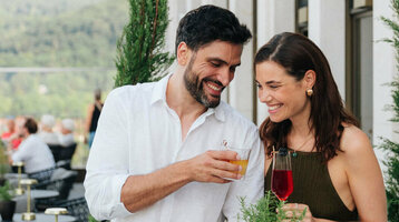 Paar genießt Getränke auf der Terrasse des ATLANTIC Hotel Heidelberg mit Blick auf grüne Hügel.