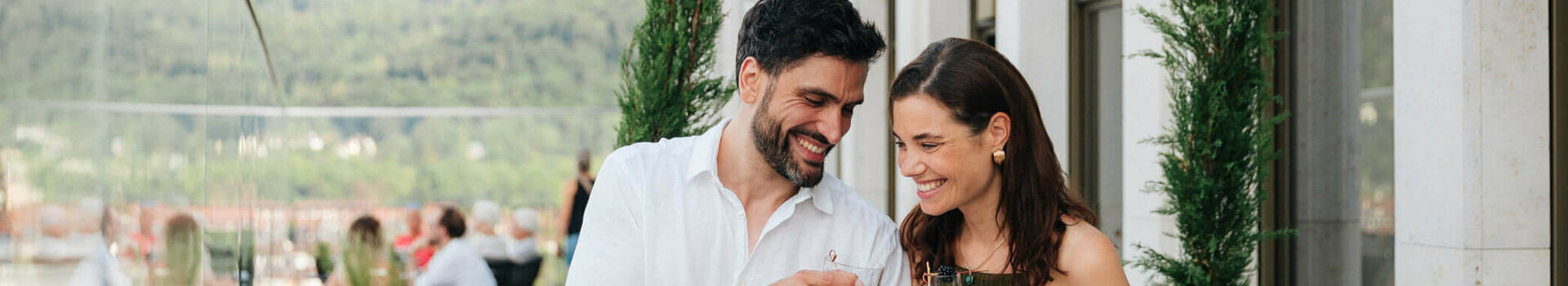 ATLANTIC Hotel Heidelberg Heidelberg entdecken Couple enjoying drinks on the terrace of the ATLANTIC Hotel Heidelberg with a view of green hills.