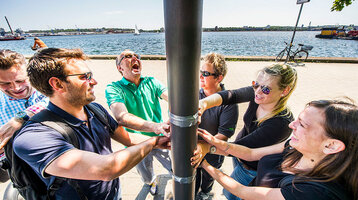 Eine Gruppe lachender Menschen steht am Kai in Kiel und fasst gemeinsam eine Laterne an.