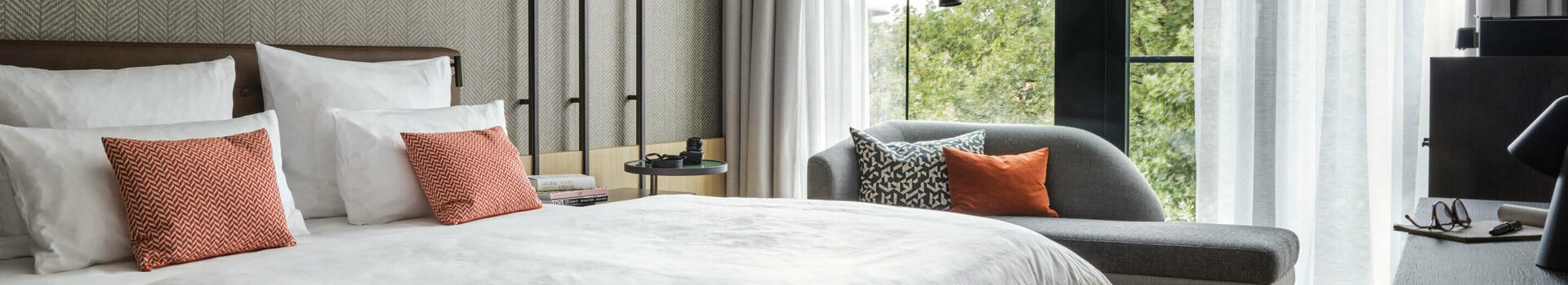 Comfort Zimmer in ATLANTIC Hotel Münster Modernes Hotelzimmer mit Doppelbett, Sofa, Schreibtisch und großen Fenstern mit Blick ins Grüne.