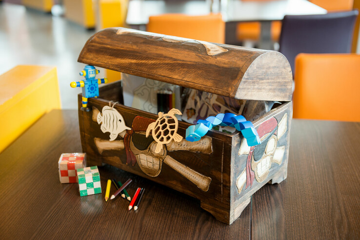 Holztruhe mit Spielzeug und Buntstiften auf Tisch in hellem Raum.