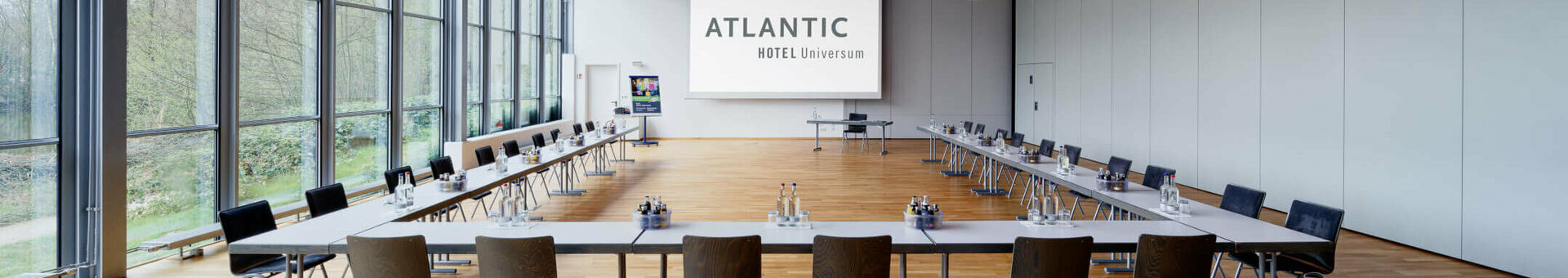Moderner Konferenzraum im ATLANTIC Hotel Universum mit großen Fenstern, U-förmiger Bestuhlung und stilvollen Deckenleuchten.