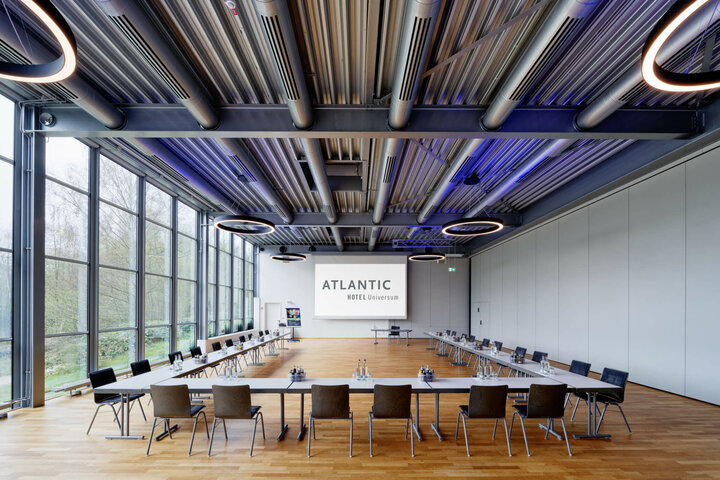 Moderner Konferenzraum im ATLANTIC Hotel Universum mit großen Fenstern, U-förmiger Bestuhlung und stilvollen Deckenleuchten.