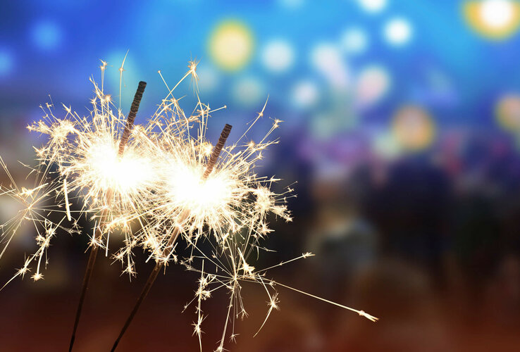 Two burning sparklers in front of a blurred, colorful background.