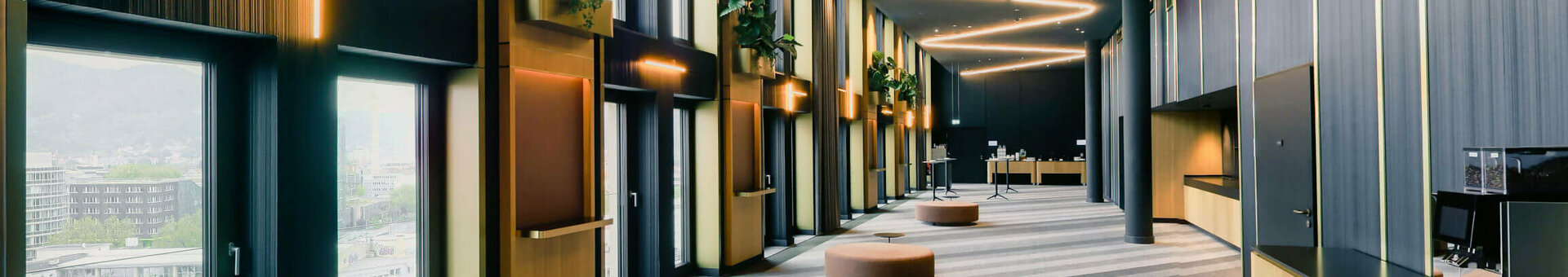 Modern hotel corridor with large windows, curved lighting, plants and seating in the ATLANTIC Hotel Heidelberg.