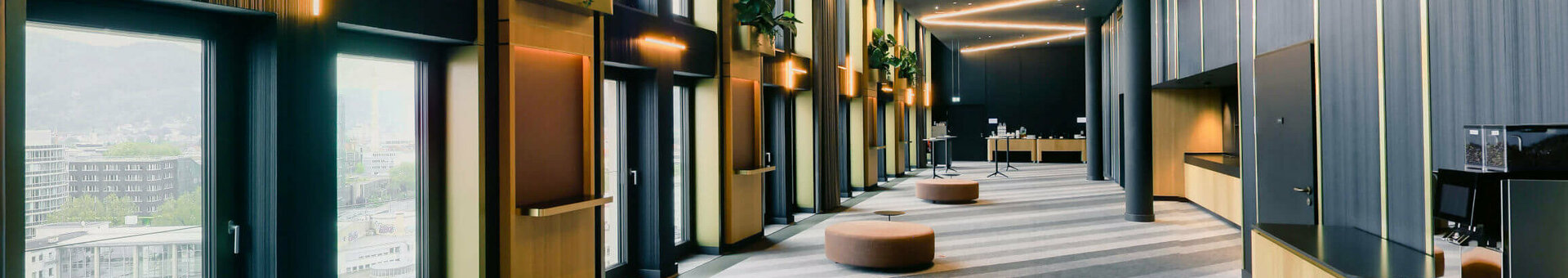 ATLANTIC Hotel Heidelberg Foyer Moderner Hotelflur mit großen Fenstern, geschwungener Beleuchtung, Pflanzen und Sitzgelegenheiten im ATLANTIC Hotel Heidelberg.