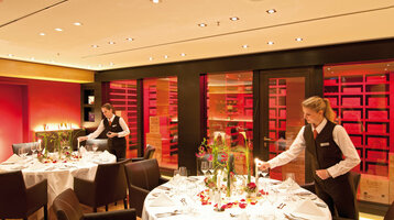 Weinkeller im ATLANTIC Hotel Kiel Elegantes Restaurant im ATLANTIC Hotel Kiel, gedeckte Tische, warme Beleuchtung, Personal richtet Tische her.