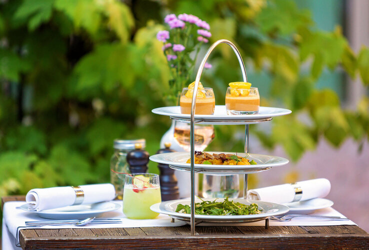 Set table with three-tiered etagere, with appetizers on top, in the garden of the ATLANTIC Grand Hotel Bremen.