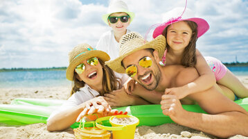 ATLANTIC Grand Hotel Travemünde – Family at the beach Family on the beach with sun hats and sunglasses, laughing on an air mattress, sand toys in the foreground.