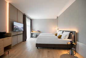 Modernes Hotelzimmer mit Doppelbett, Schreibtisch, Flachbild-TV und großen Fenstern im ATLANTIC Hotel Heidelberg.
