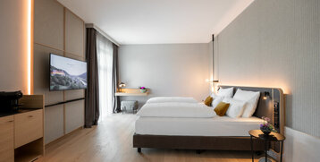 Modern hotel room with double bed, desk, flat-screen TV and large windows at the ATLANTIC Hotel Heidelberg.