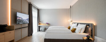 Modernes Hotelzimmer mit Doppelbett, Schreibtisch, Flachbild-TV und großen Fenstern im ATLANTIC Hotel Heidelberg.