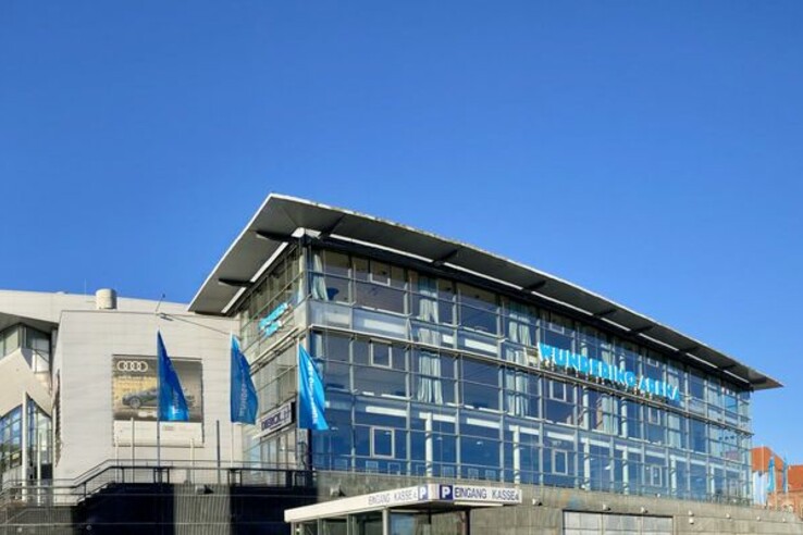 Modern building with glass façade and blue sky, next to a historic church tower.