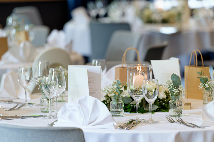 Ein eingedeckter Tisch bei einer Hochzeit mit weißer Tischdecke, gefächerten Servietten, Schleierkraut und weißen Rosen.