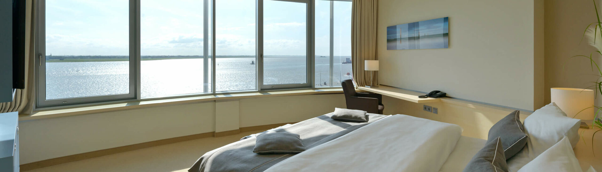 Interior view of the Suite in the ATLANTIC Hotel SAIL City in Bremerhaven with an amazing view over the Weser Bright hotel room with large bed and panoramic window overlooking the water.