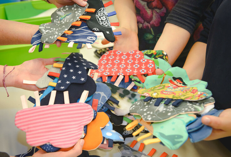 Several hands hold colorful, cloud-shaped fabric toys with different patterns.