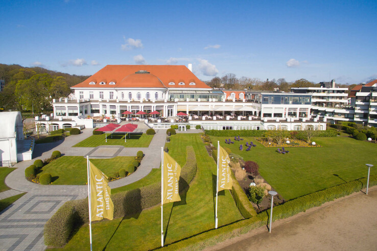 ATLANTIC Grand Hotel Travemünde mit gepflegtem Garten, Rasenflächen, Flaggen und Terrasse unter blauem Himmel.