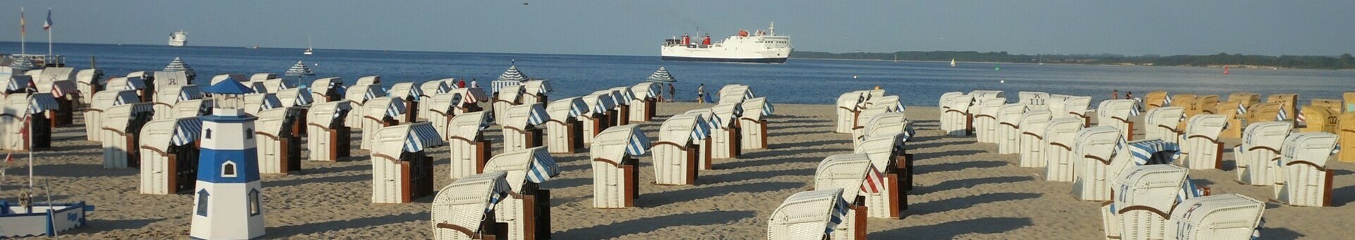 Strand mit vielen Strandkörben, Blick auf die Ostsee und ein vorbeifahrendes Schiff bei sonnigem Wetter.