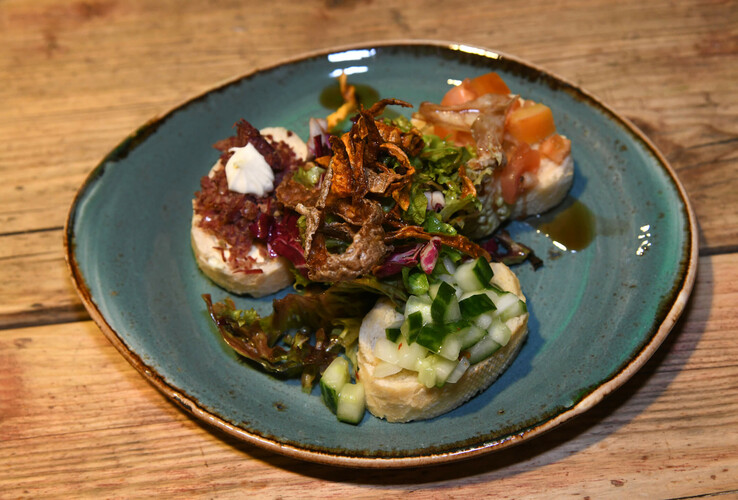 Vorspeisenteller mit Brot, frischem Salat, Gurken, Tomaten und knusprigen Toppings auf rustikalem Holztisch.