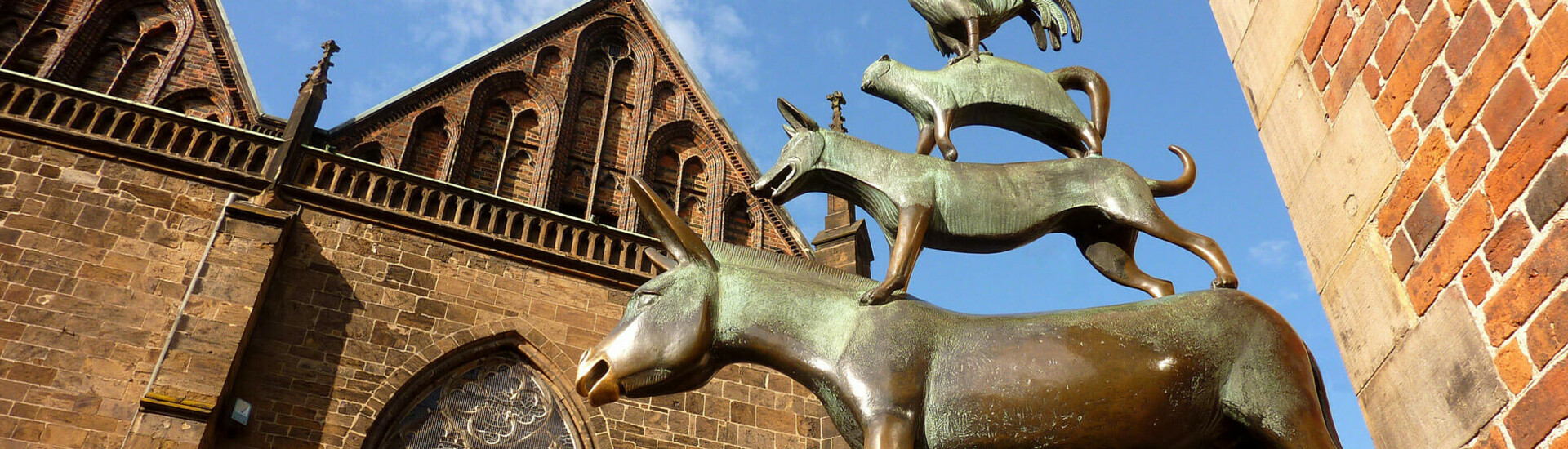 Bronzestatue der Bremer Stadtmusikanten vor historischer Backsteinfassade, blauer Himmel im Hintergrund.