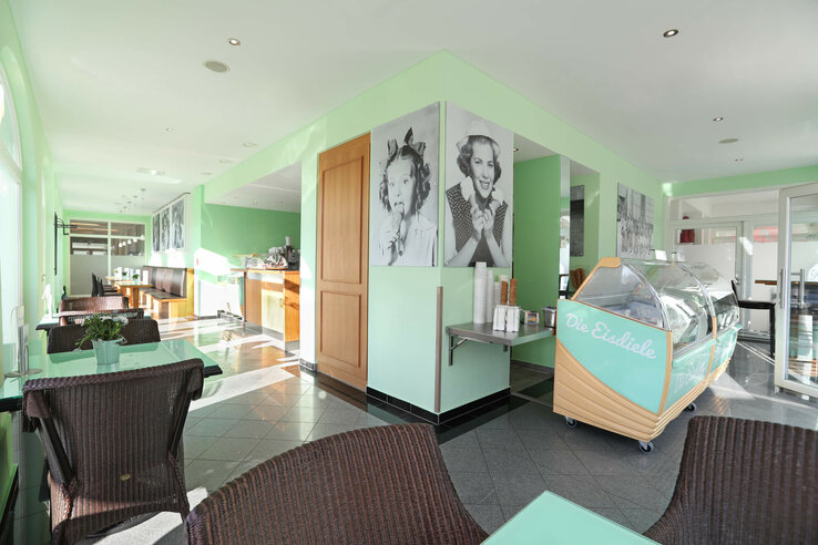 Helles Eiscafé mit grünen Wänden, Eistheke, Korbstühlen und Schwarz-Weiß-Fotos an den Wänden im ATLANTIC Grand Hotel.