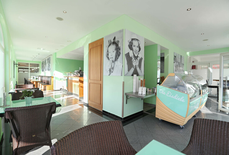 Helles Eiscafé mit grünen Wänden, Eistheke, Korbstühlen und Schwarz-Weiß-Fotos an den Wänden im ATLANTIC Grand Hotel.