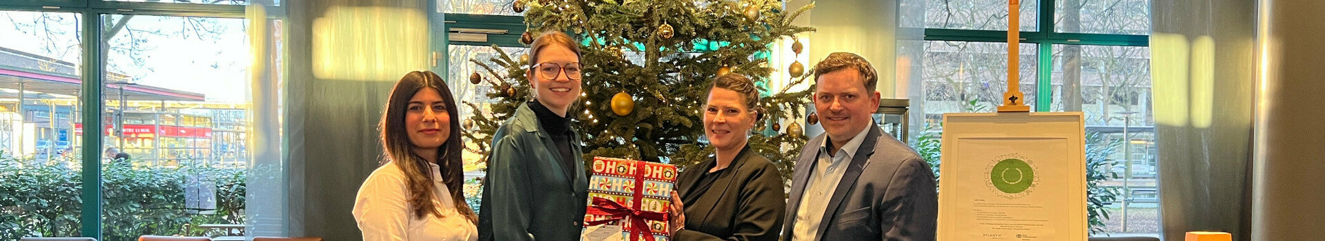 4 Personen stehen vor einem Weihnachtsbaum mit vielen Geschenken