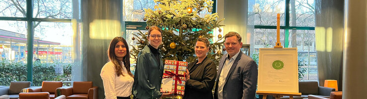 4 Personen stehen vor einem Weihnachtsbaum mit vielen Geschenken