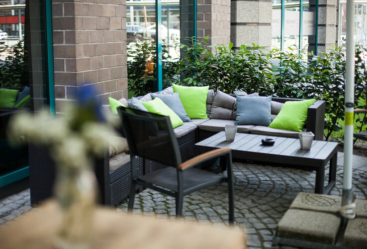 Cozy outdoor terrace with seating area, colorful cushions and plants at the ATLANTIC Hotel Airport Bremen.
