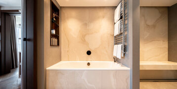 Modernes Badezimmer mit großer Badewanne, Handtuchheizkörper und eleganter Beleuchtung im ATLANTIC Hotel Heidelberg.