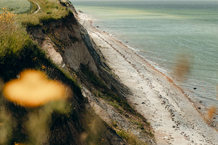 Steilküste mit grasbewachsenem Pfad und Blick auf das Meer bei bewölktem Himmel.
