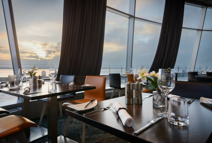 Modern restaurant with set tables, large windows and a view of the sunset over the water in the ATLANTIC Hotel.