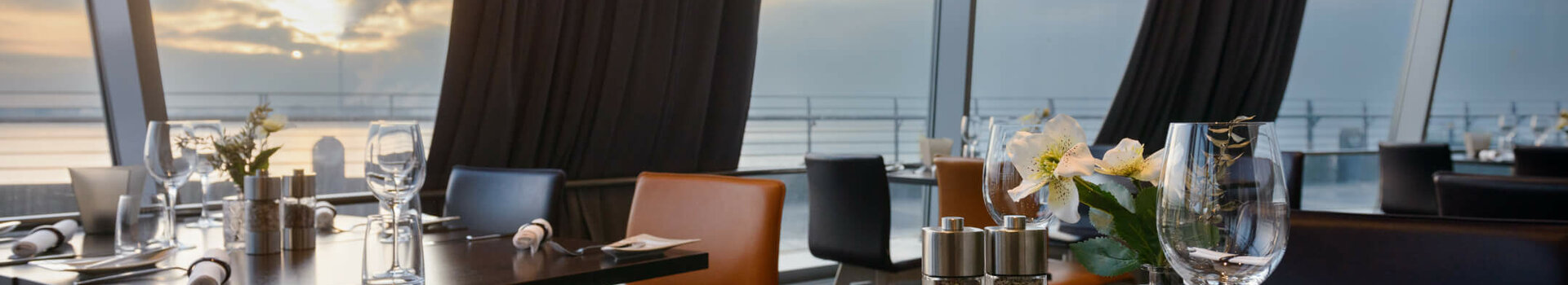 Modernes Restaurant mit gedeckten Tischen, großen Fenstern und Blick auf Sonnenuntergang über dem Wasser im ATLANTIC Hotel.