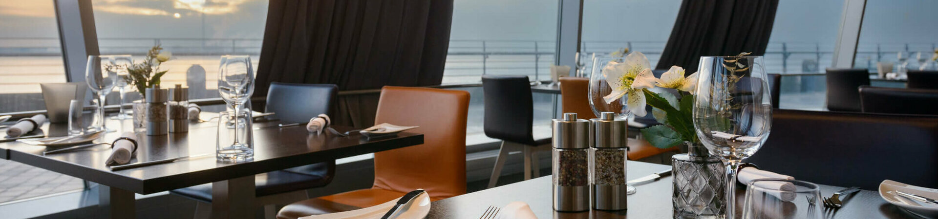 Modernes Restaurant mit gedeckten Tischen, großen Fenstern und Blick auf Sonnenuntergang über dem Wasser im ATLANTIC Hotel.