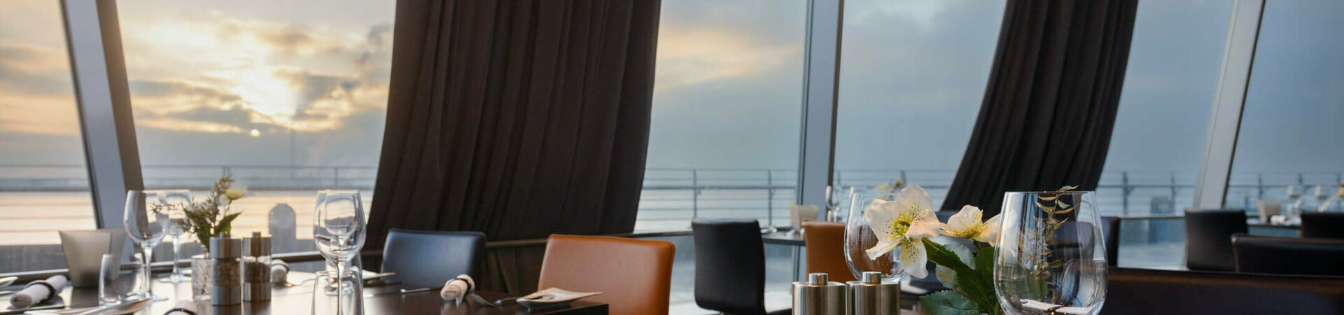 Modern restaurant with set tables, large windows and a view of the sunset over the water in the ATLANTIC Hotel.