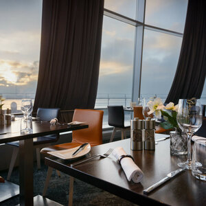 Modernes Restaurant mit gedeckten Tischen, großen Fenstern und Blick auf Sonnenuntergang über dem Wasser im ATLANTIC Hotel.