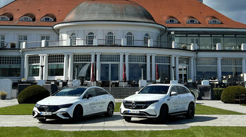 Historisches Hotelgebäude mit rotem Dach, davor zwei weiße Autos auf gepflegtem Rasen unter blauem Himmel.
