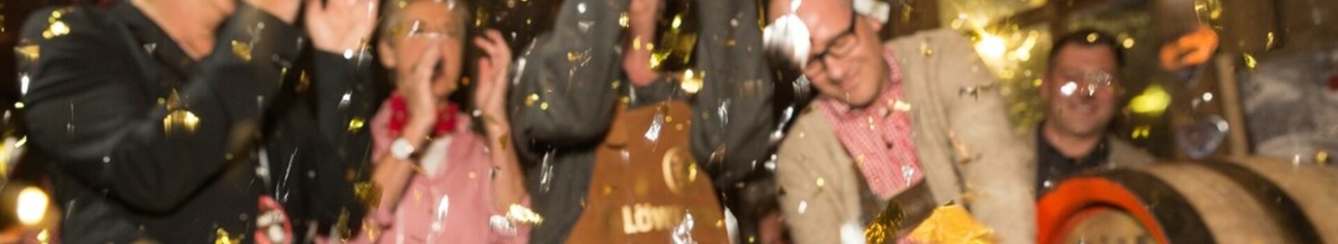 ATLANTIC Grand Hotel Bremen – Almhütte Menschen feiern in traditioneller Kleidung, während ein Mann ein Bierfass anschlägt, umgeben von Konfetti.