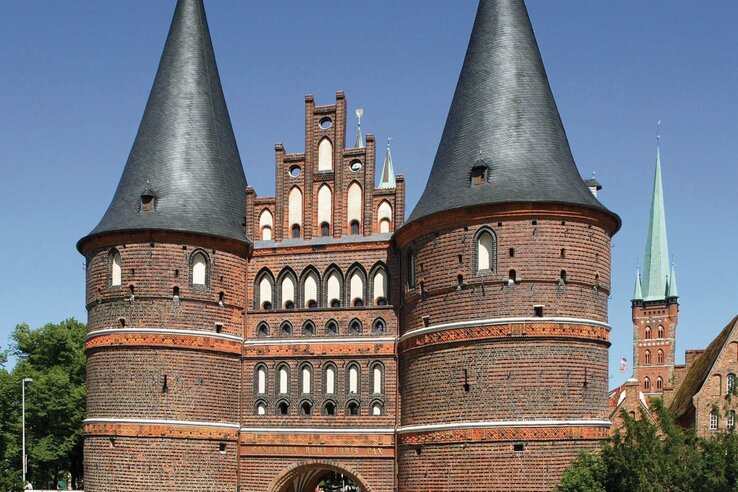 Backsteingotik-Holstentor mit zwei Rundtürmen und grünem Rasen im Vordergrund, blauer Himmel im Hintergrund.