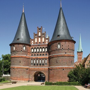 Backsteingotik-Holstentor mit zwei Rundtürmen und grünem Rasen im Vordergrund, blauer Himmel im Hintergrund.