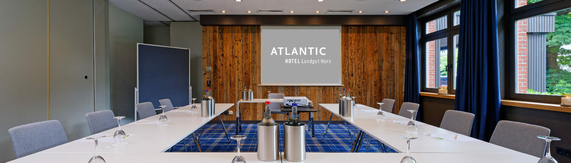 Modern conference room with U-shaped table, projector and wooden wall at the ATLANTIC Hotel Landgut Horn Bremen.