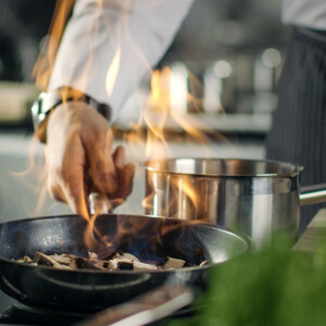 Chef in action: Flambéed mushrooms in a pan next to a saucepan in a modern hotel kitchen.