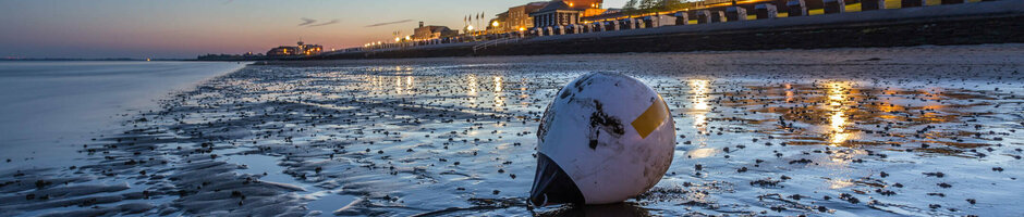 Beach at sunset with buoy in the foreground and illuminated hotel in the background.