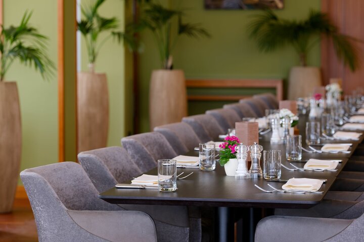 Eleganter Restauranttisch mit grauen Stühlen, stilvoll gedeckt, umgeben von grünen Pflanzen in einem modernen Ambiente.